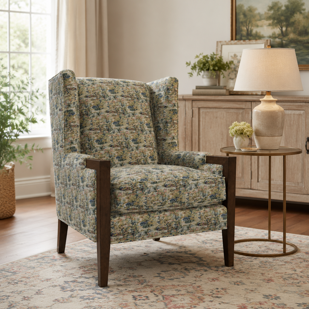 Patterned tapestry wingback armchair with dark wooden arms set on an area rug beside a small side table and lamp.
