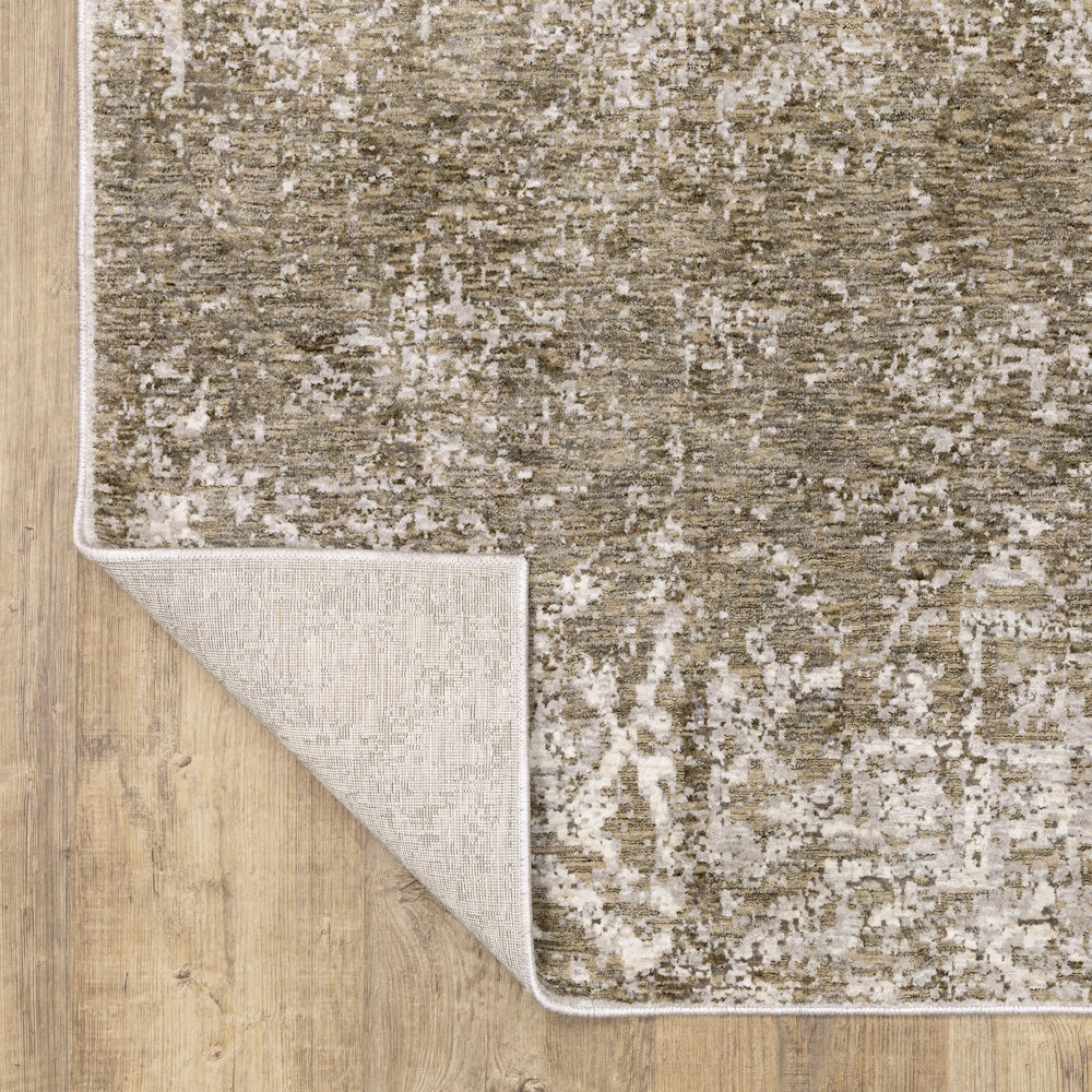 Corner of the gray, taupe, and cream area rug folded back to show the backing material on a wooden floor.