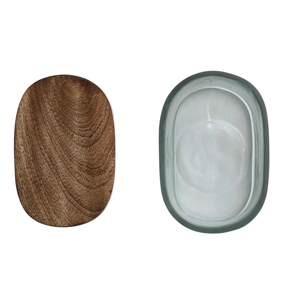 Top view of an oval hand-blown glass jar next to its natural mango wood lid, showing wood grain and clear glass texture.