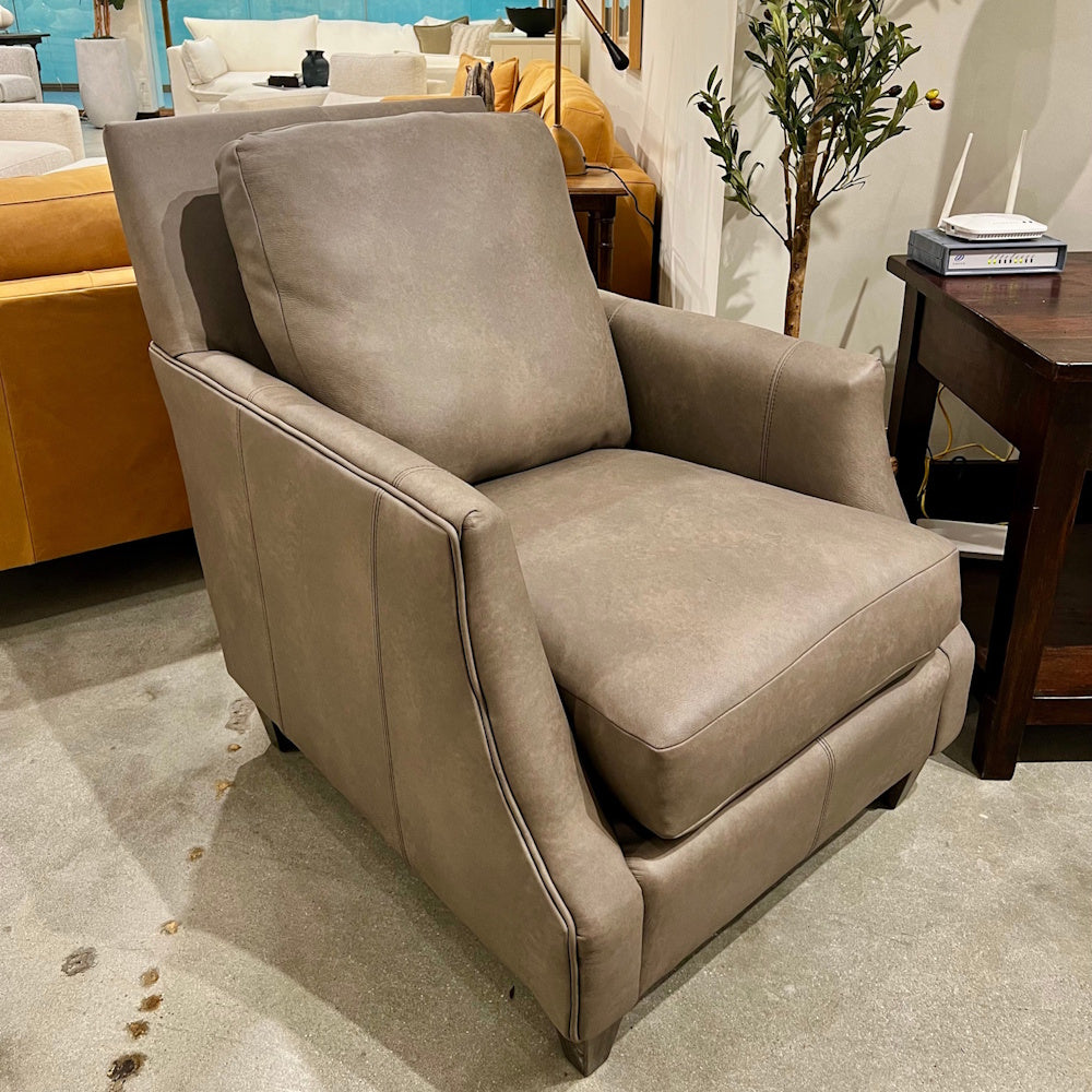 Grey leather armchair with plush back cushion displayed on a showroom floor next to a side table.