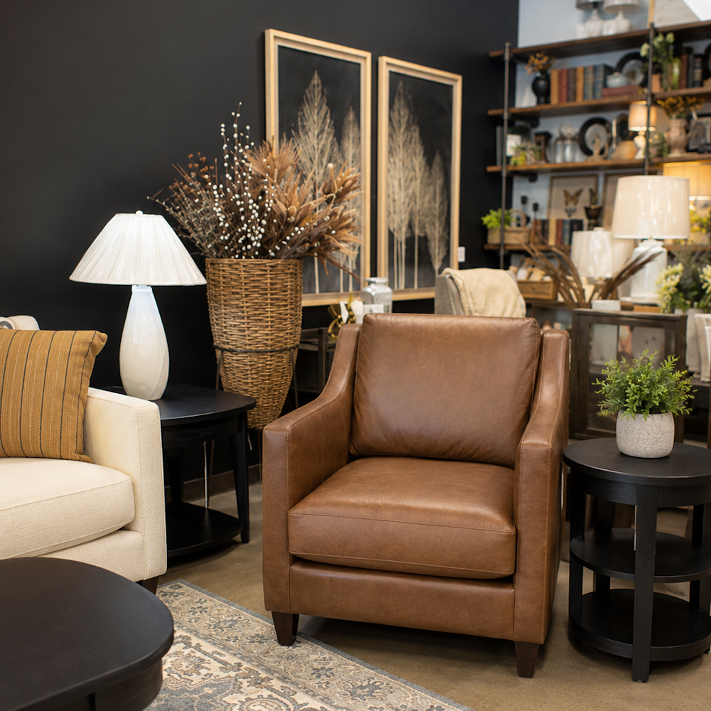 Brown leather accent chair in styled living room with loose cushions, tapered legs and box arms.