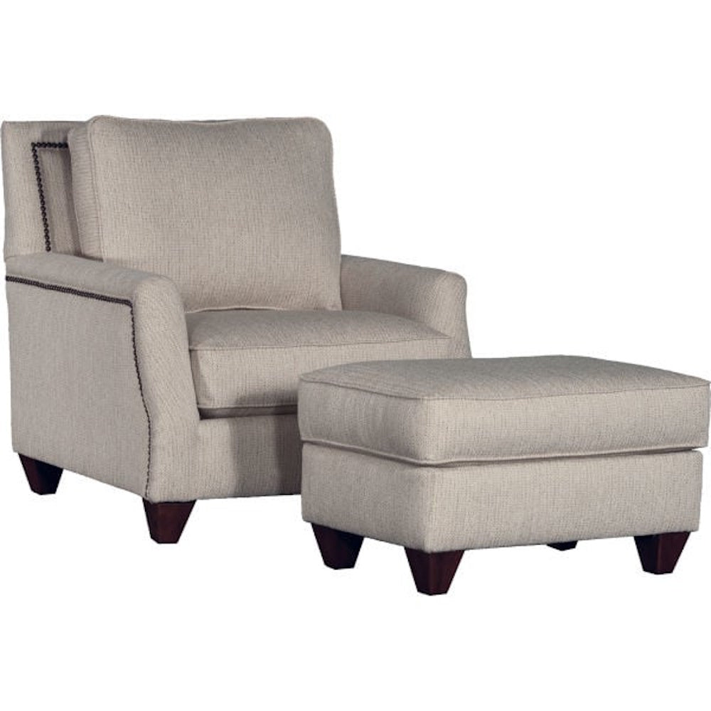 Beige nailhead trim armchair with matching ottoman and dark wood feet.