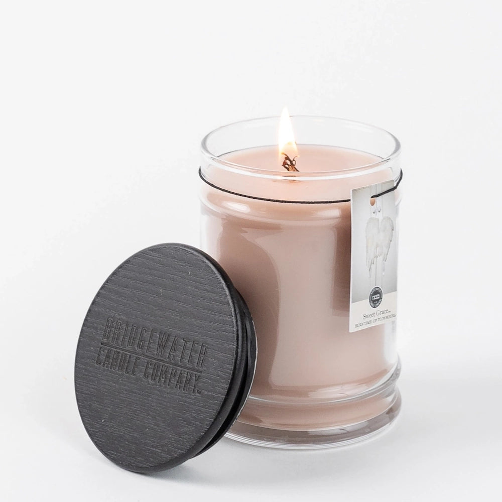 Lit jar candle with blush pink wax, a black wooden lid resting beside it, and a white background.