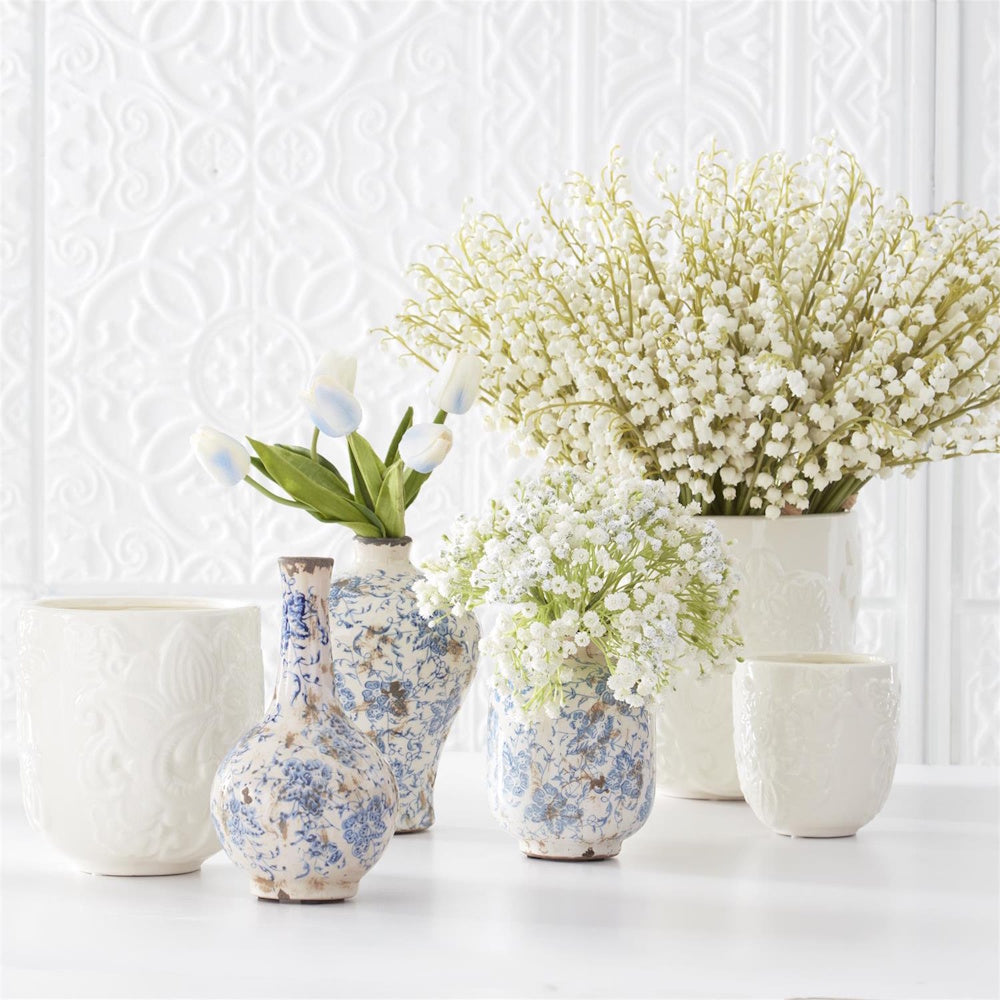 White lily of the valley and blue tulips in vintage blue and white ceramic vases against a white textured wall.
