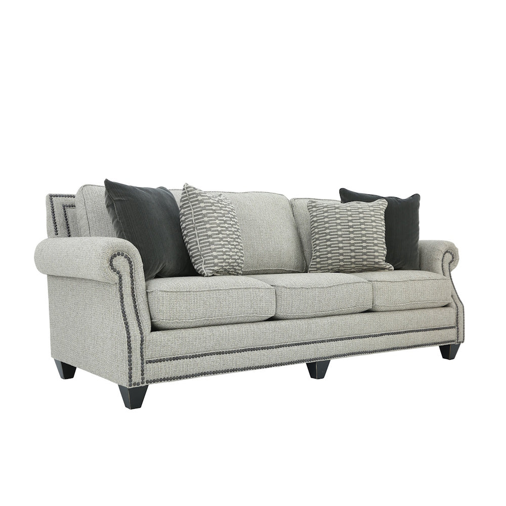 Three-quarter view of a light gray sofa with rolled arms, nailhead trim, and throw pillows.