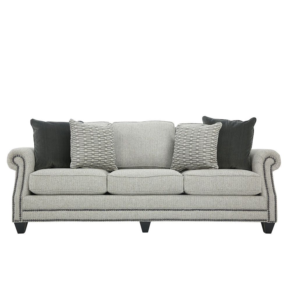 Light gray three-cushion sofa with rolled arms, nailhead trim, and throw pillows.