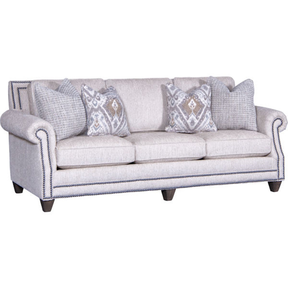 Light gray upholstered sofa with nailhead trim detailing and patterned throw pillows.