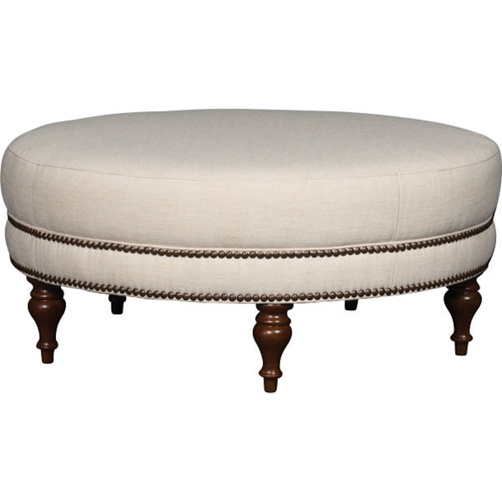 Round beige upholstered ottoman with nailhead trim and turned wooden legs on a white background.