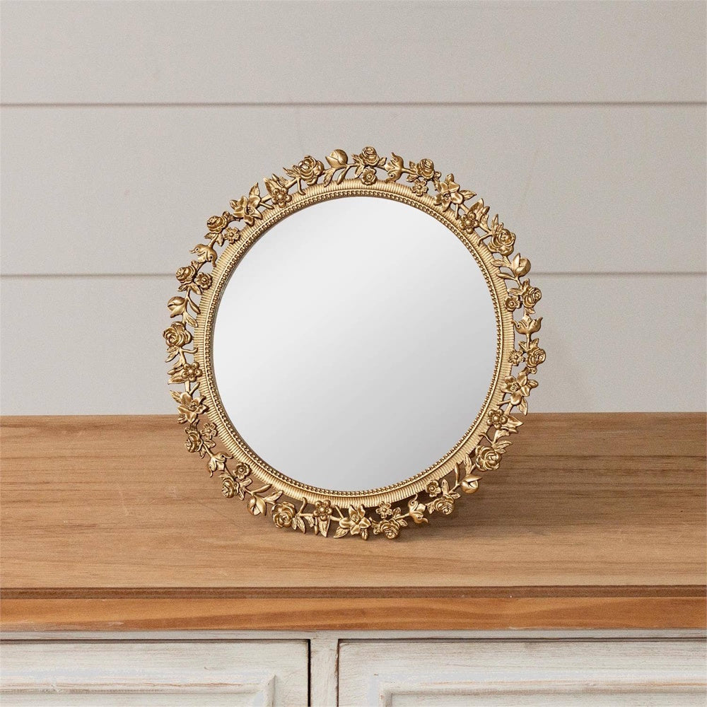 Gold floral round table mirror with ornate rose frame on a wooden dresser against a white shiplap wall.