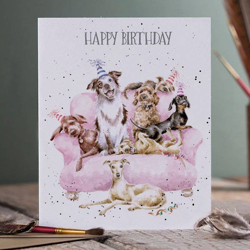 A watercolor birthday card featuring various dogs in party hats sitting on a pink sofa with "Happy Birthday" text.