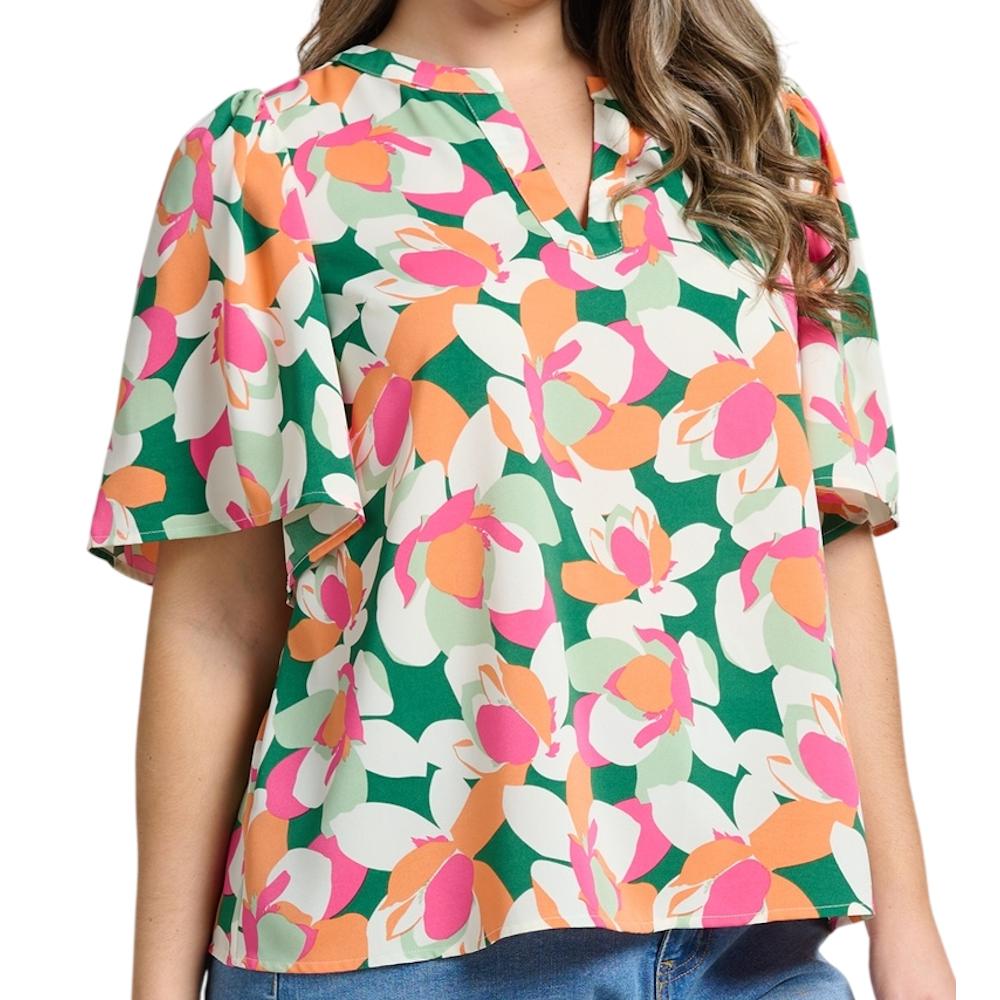 Woman wearing a short-sleeve blouse with a vibrant green, pink, and orange abstract floral print.
