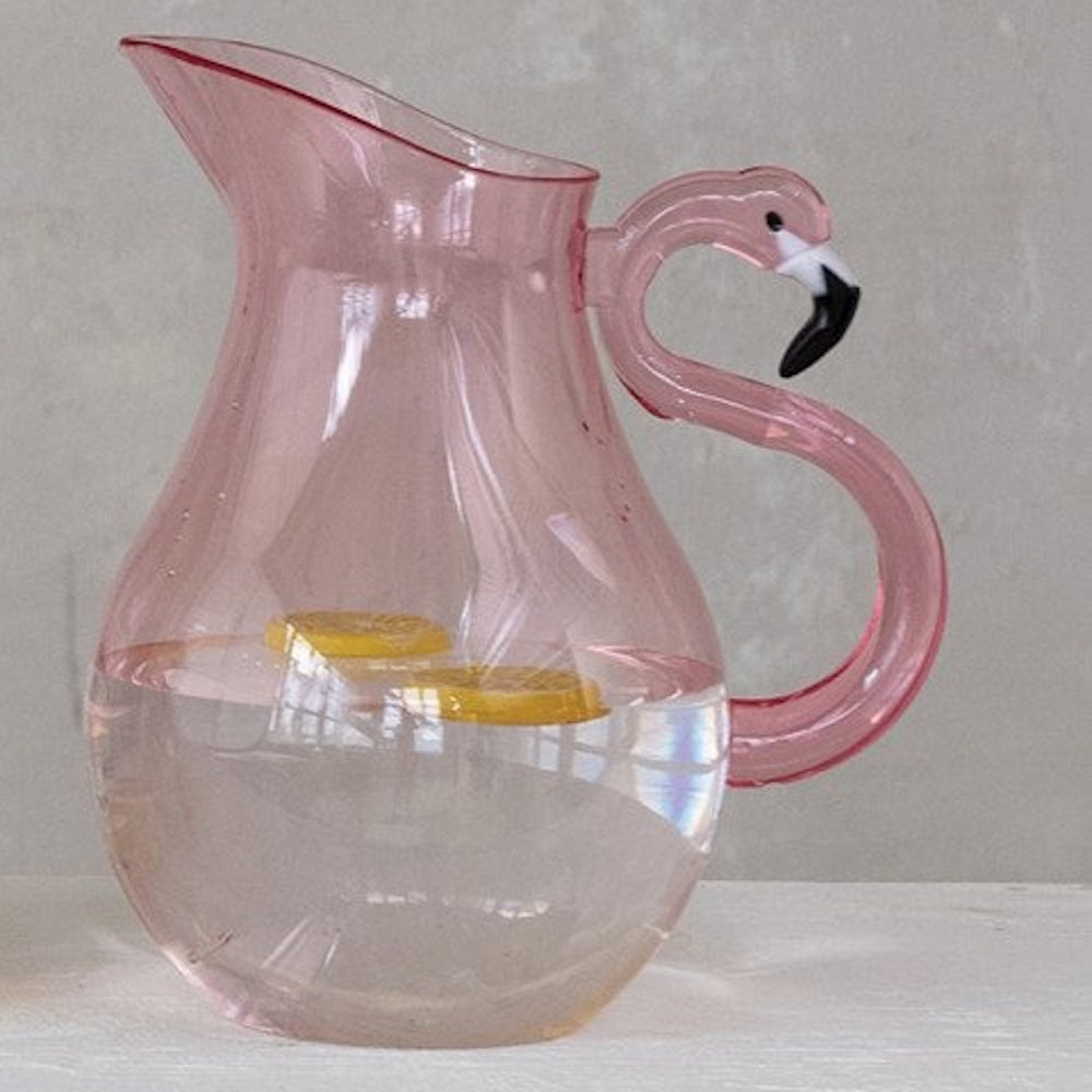 A pink glass pitcher filled with water and lemon slices, featuring a handle shaped like a flamingo.