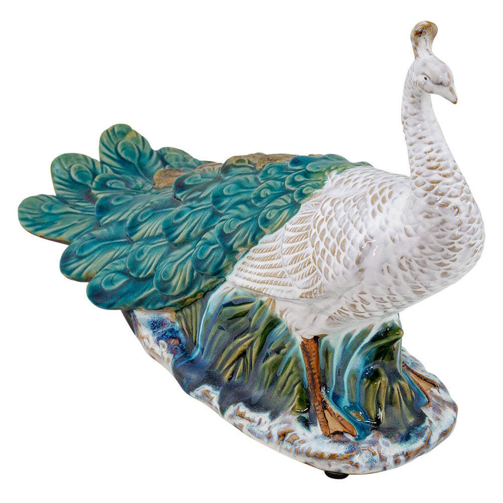 Ceramic peacock figurine with a white neck, teal and green feathered tail, and a glazed blue base.