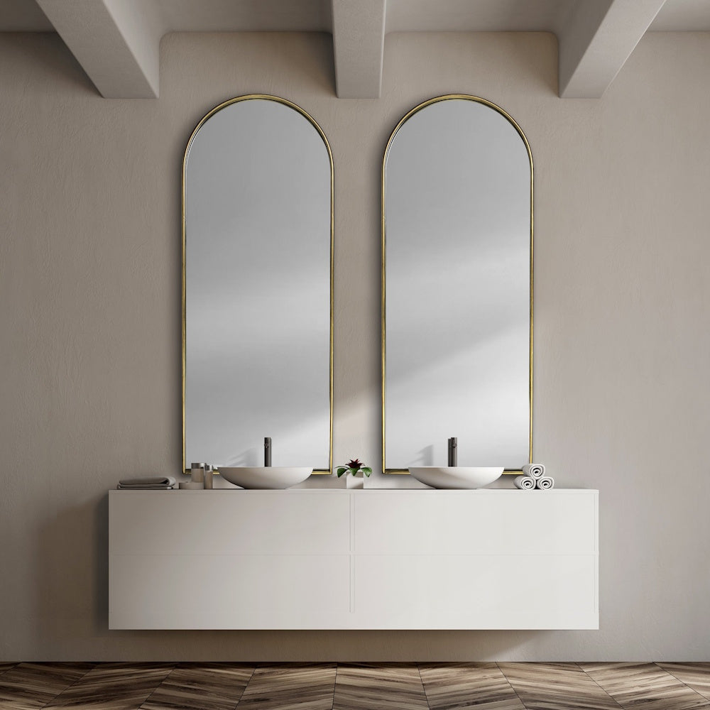 Two arched gold mirrors mounted above a floating white double-vanity bathroom sink.