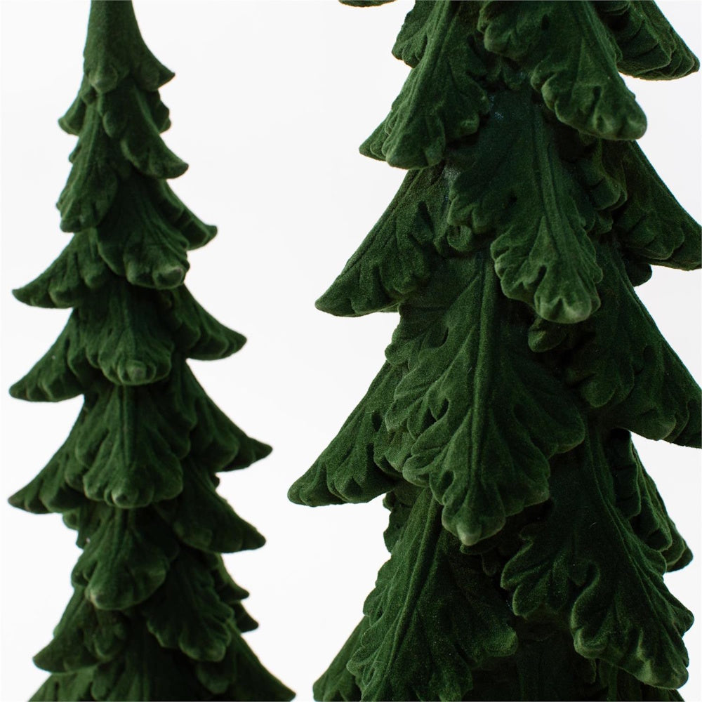 Close-up of two dark green flocked miniature alpine fir trees against a white background.