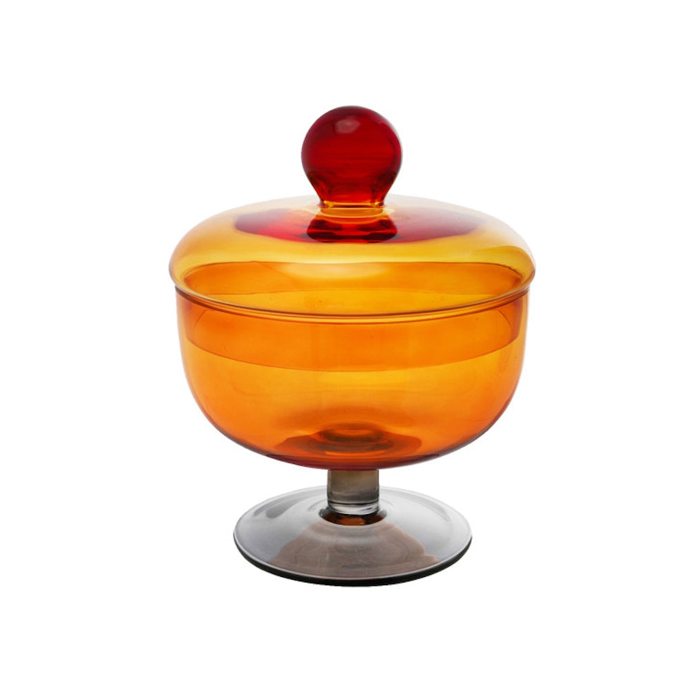 An amber glass footed jar with a matching lid topped by a vibrant red spherical knob.