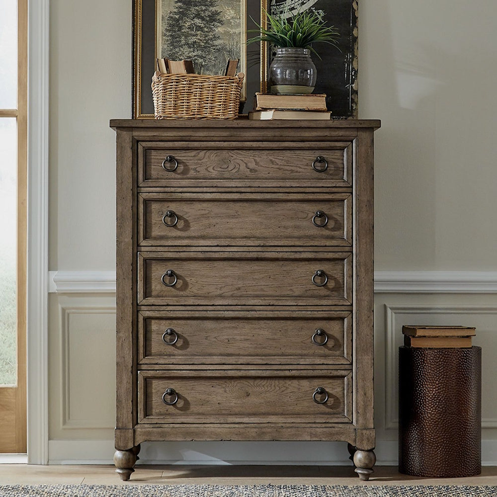 Brown wooden 5-drawer chest styled in a room with framed art, books, and decorative accents.