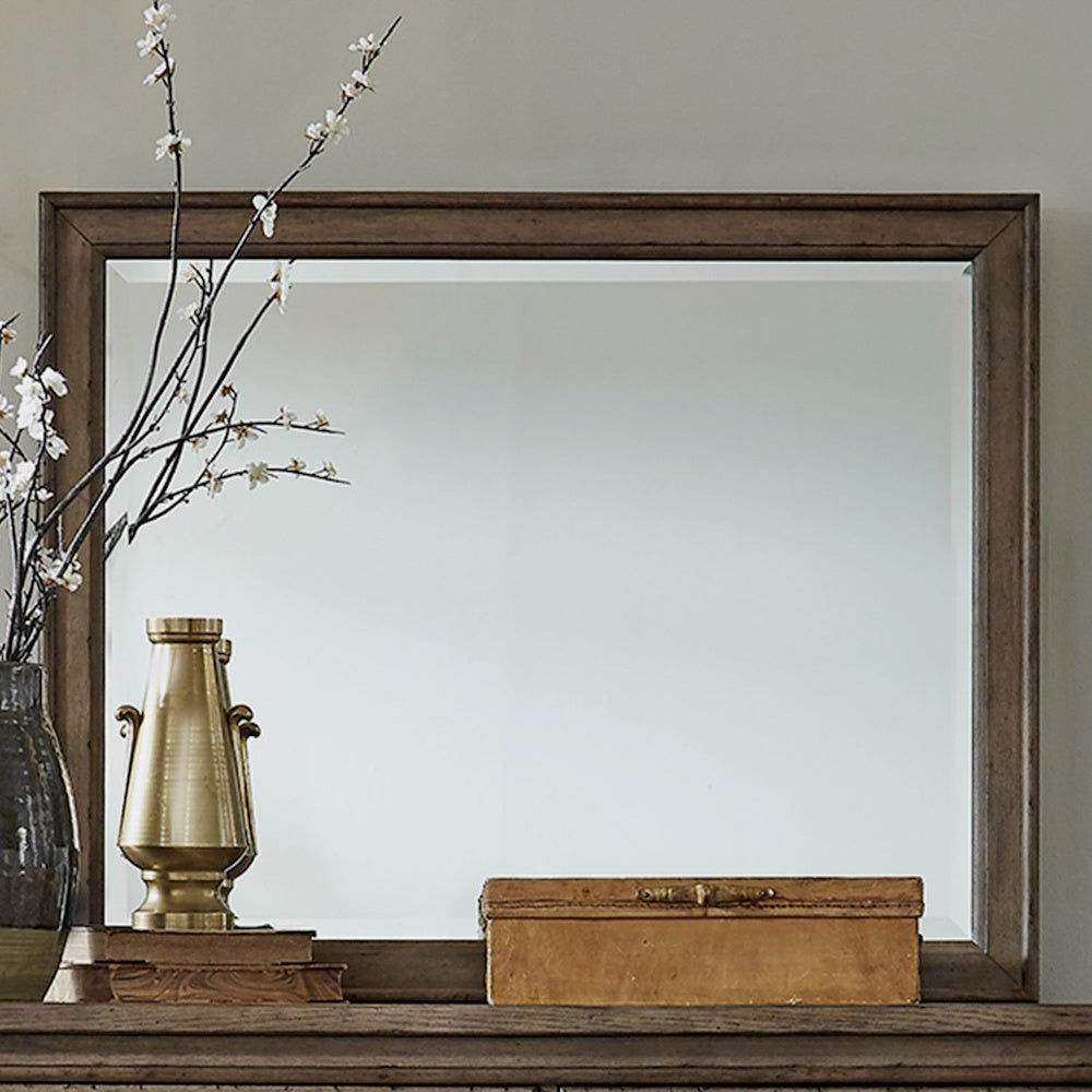 Rectangular brown wooden framed mirror styled with a brass urn, vase with branches, and small box.