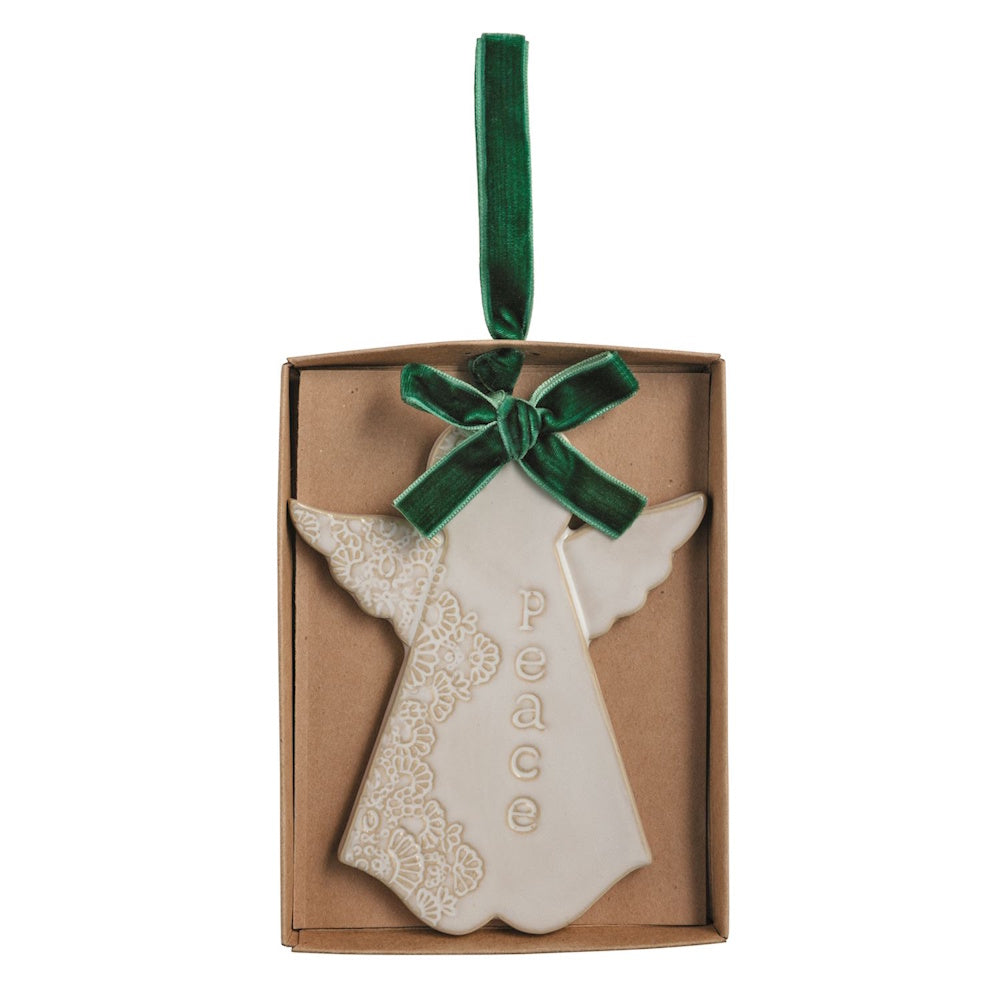 White ceramic angel ornament with green velvet ribbon and "peace" text in a cardboard box.