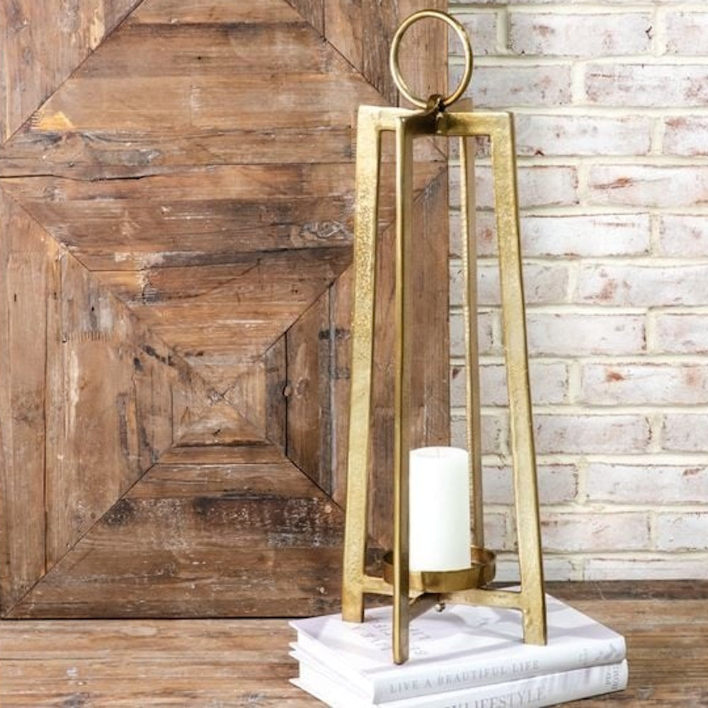 Tall antique brass open-frame candle lantern holding a white pillar candle on a stack of books.