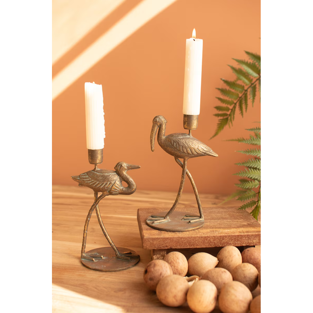 Pair of brass shorebird taper candleholders with lit candles displayed on a wooden surface.