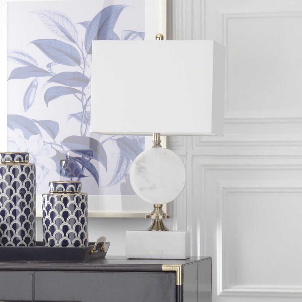Arabescato white marble table lamp with gold disc base and white rectangular shade on a dark dresser.
