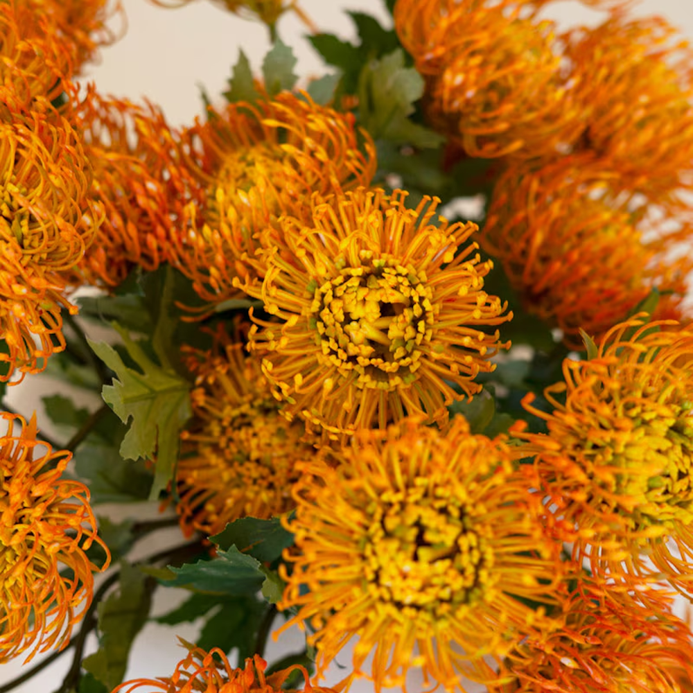 Close-up view showing the detailed texture of vibrant orange artificial pincushion protea blooms.