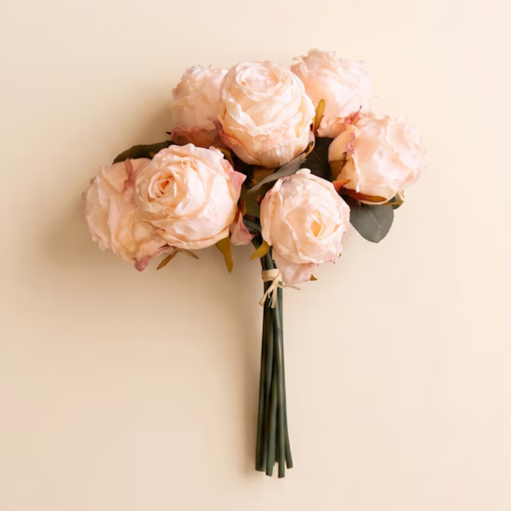 A bouquet of artificial pale pink roses tied together with twine against a neutral beige background.