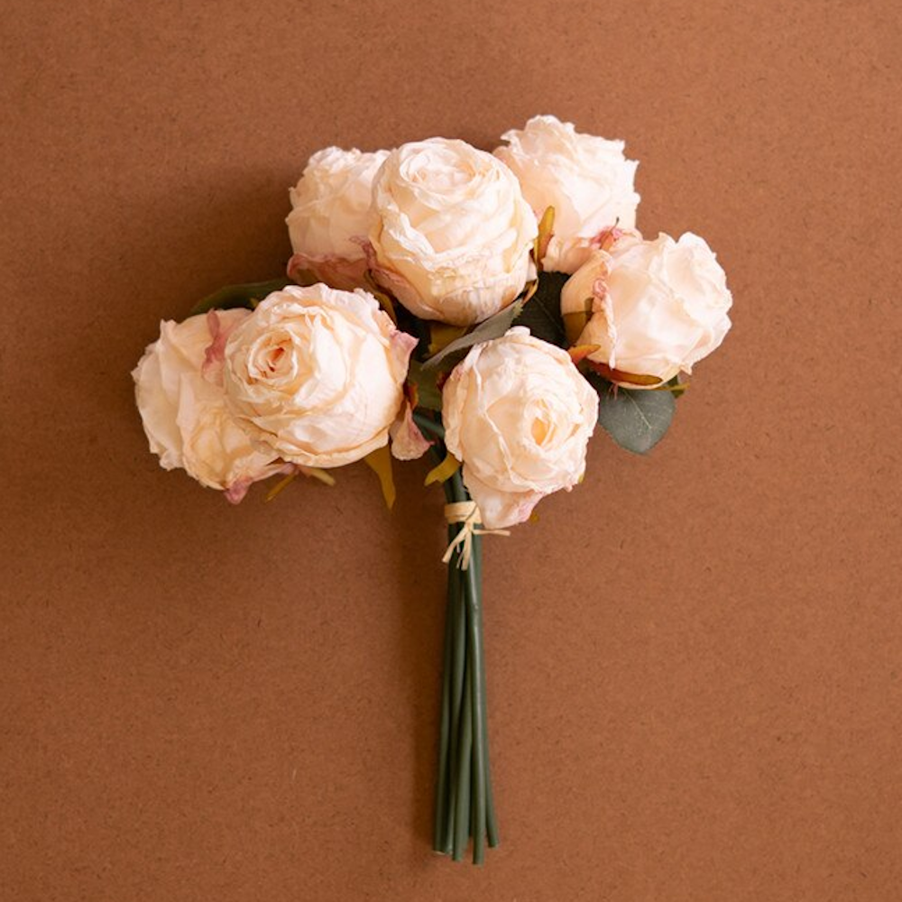 Bundle of artificial cream-colored roses tied with twine on a warm brown background.