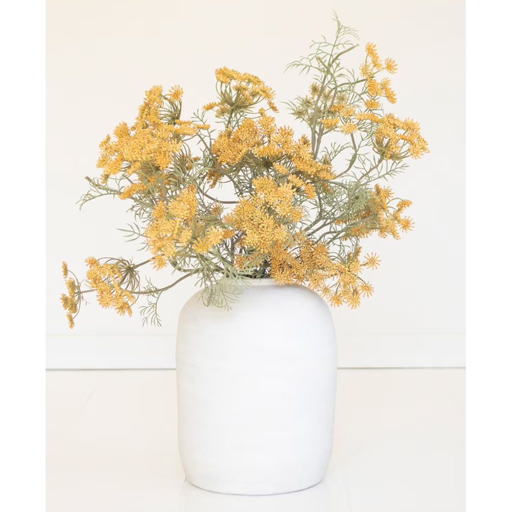 Arrangement of artificial yellow lace flowers in a simple white ceramic jar against a pale backdrop.