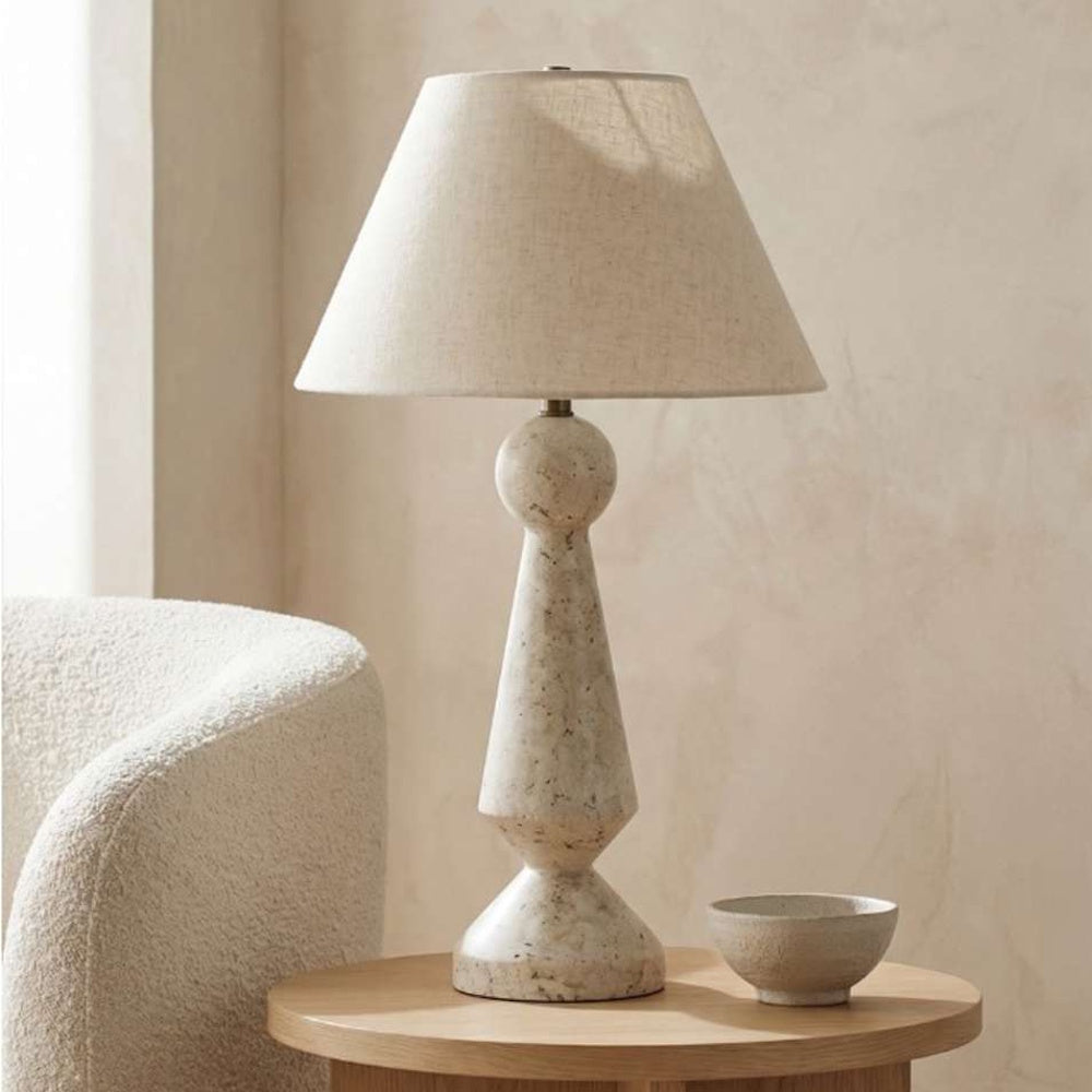 Speckled beige table lamp styled on a wooden side table next to a decorative bowl and bouclé armchair.
