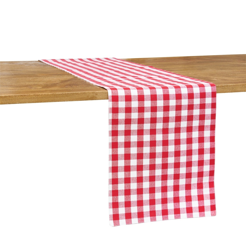 A red and white gingham check table runner draped over the edge of a light-toned wooden table against a white backdrop.