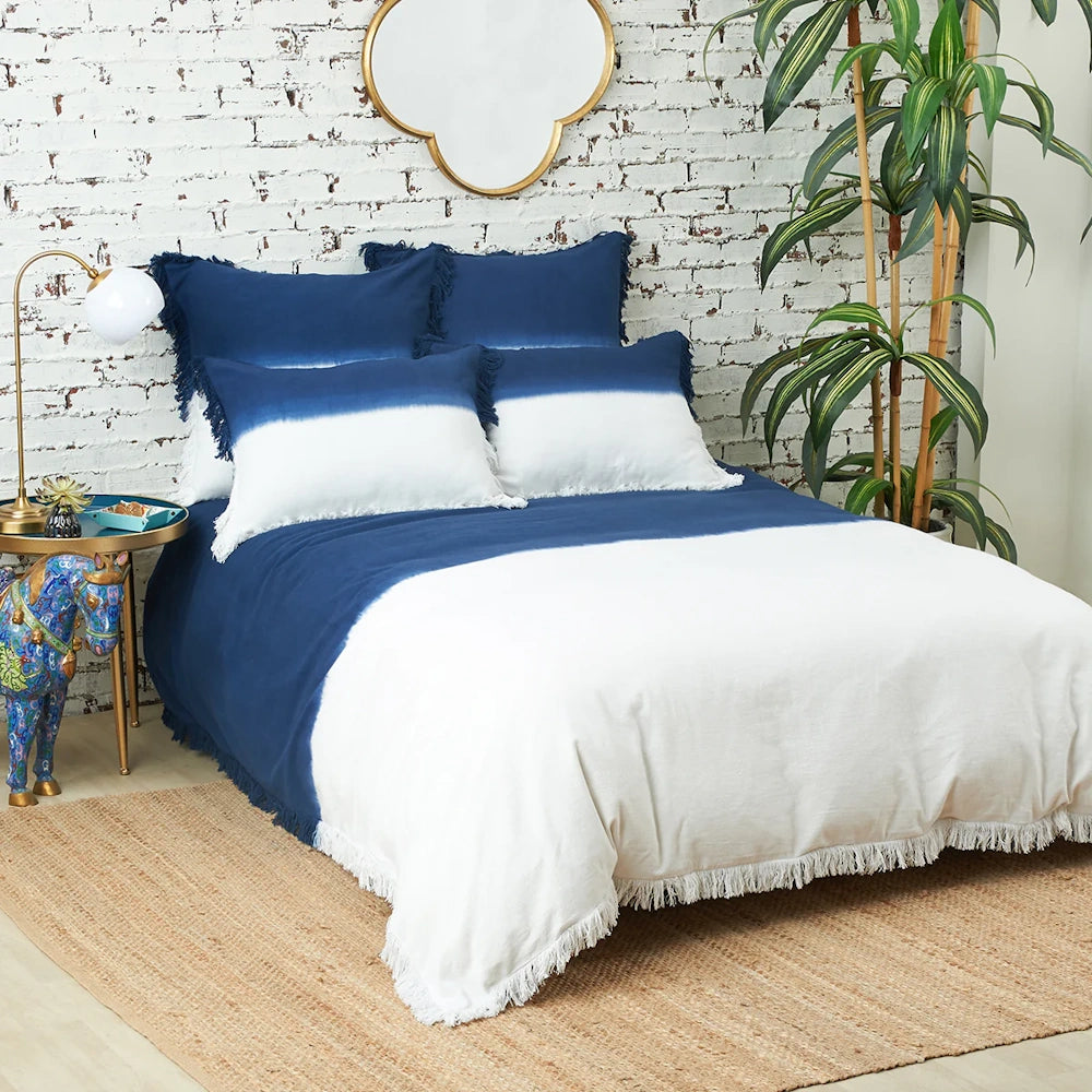 A bed with a blue and white dip-dye duvet and pillows in a bedroom with a white brick wall.