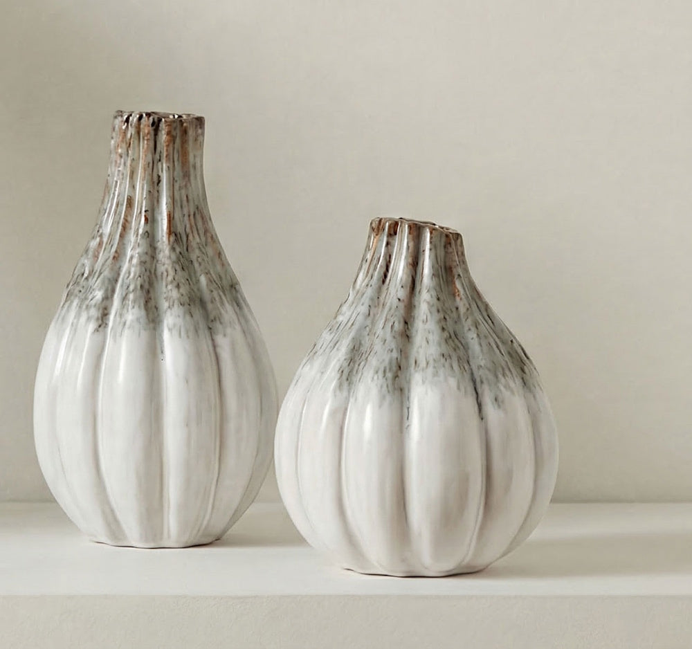 Pair of white and grey ribbed ceramic vases with a rustic glazed finish, displayed on a shelf in a neutral room.