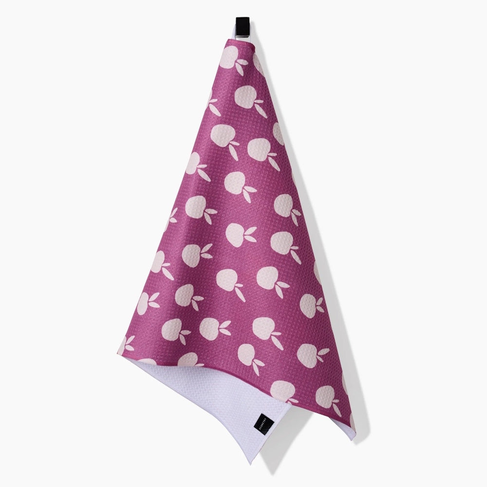 A purple tea towel with a white apple pattern hangs from a black loop against a white background.