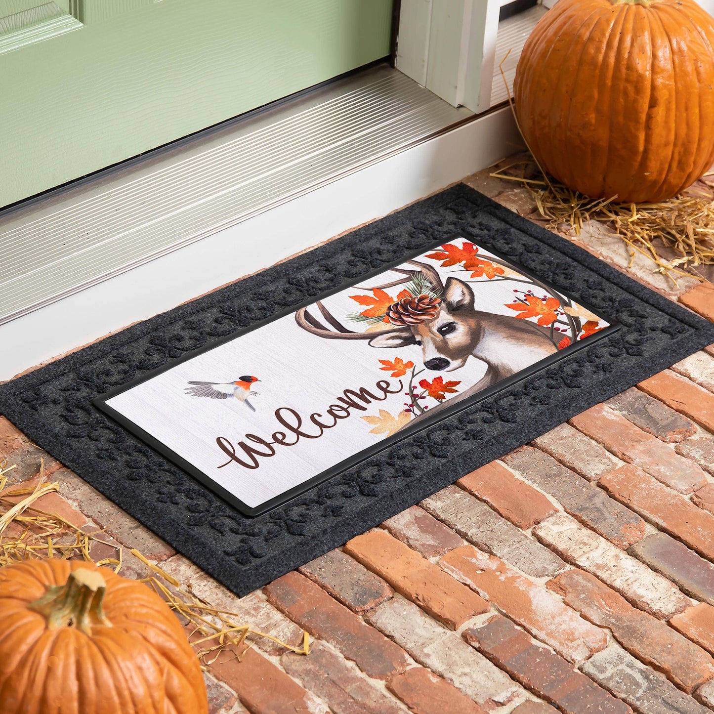 An autumn doormat with a deer, bird, and "Welcome" script, framed by pumpkins on a brick porch.