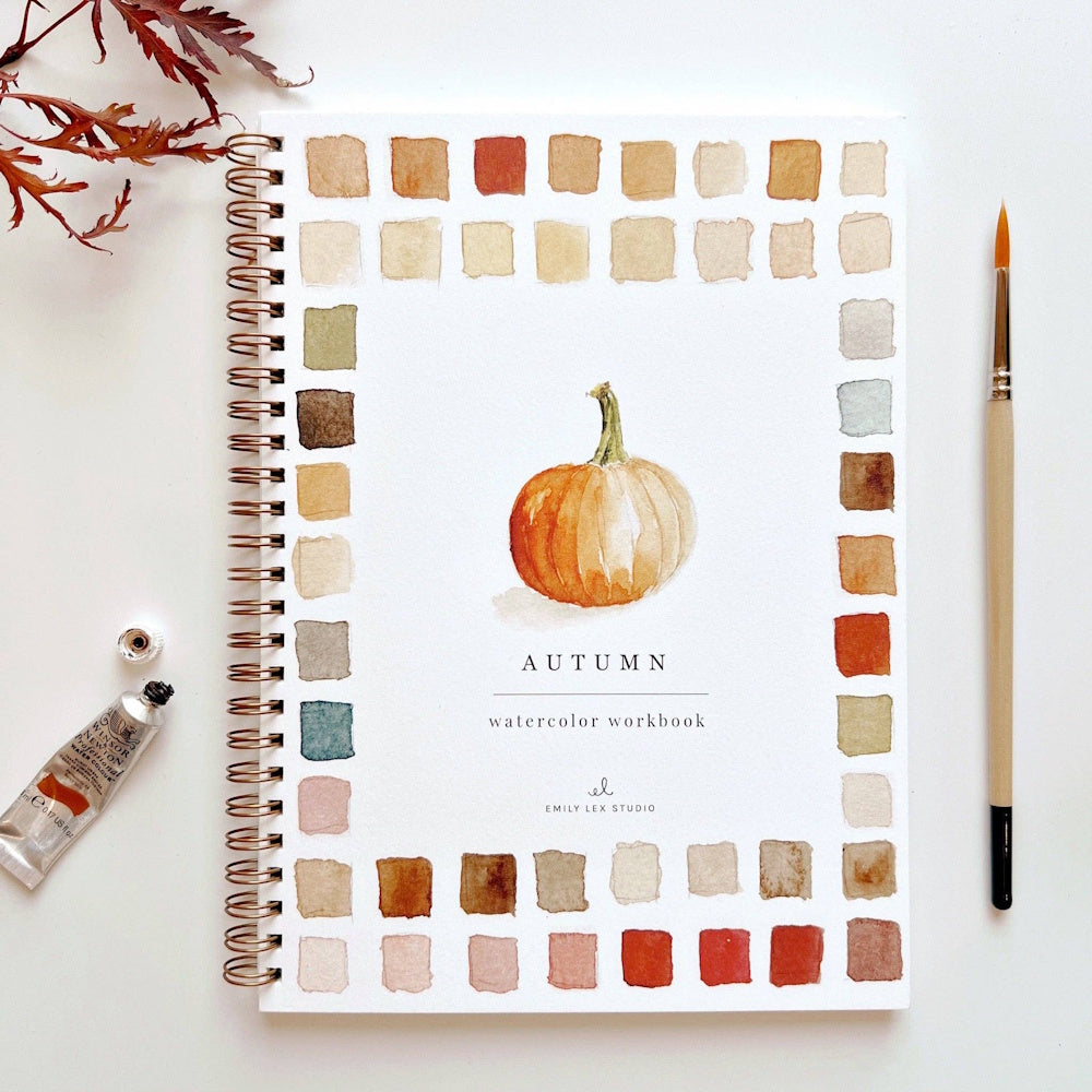 Autumn watercolor workbook with paint swatches, a pumpkin illustration, paintbrush, and paint tube.