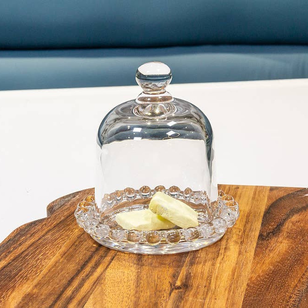 Clear glass cloche dome with beaded edge plate covering butter on wooden board.