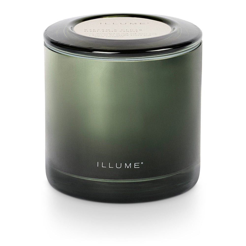 A dark green glass jar candle with its lid on and ILLUME branding on the front.
