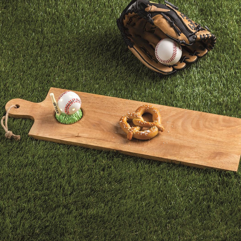 Baseball themed wooden serving board with pretzel and salt on green grass next to a glove and ball.