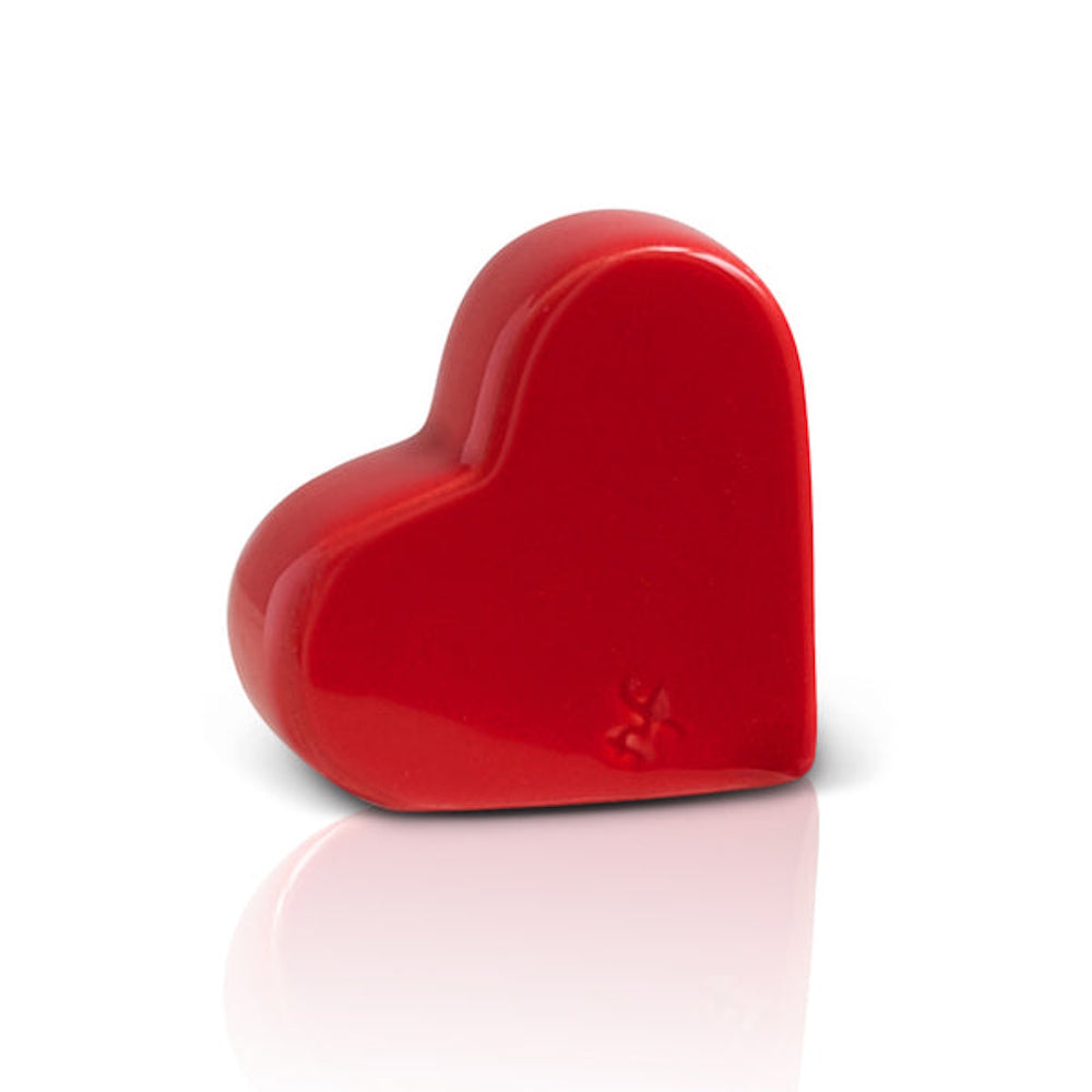 A glossy, three-dimensional red ceramic heart stands upright on a white background with a soft reflection.