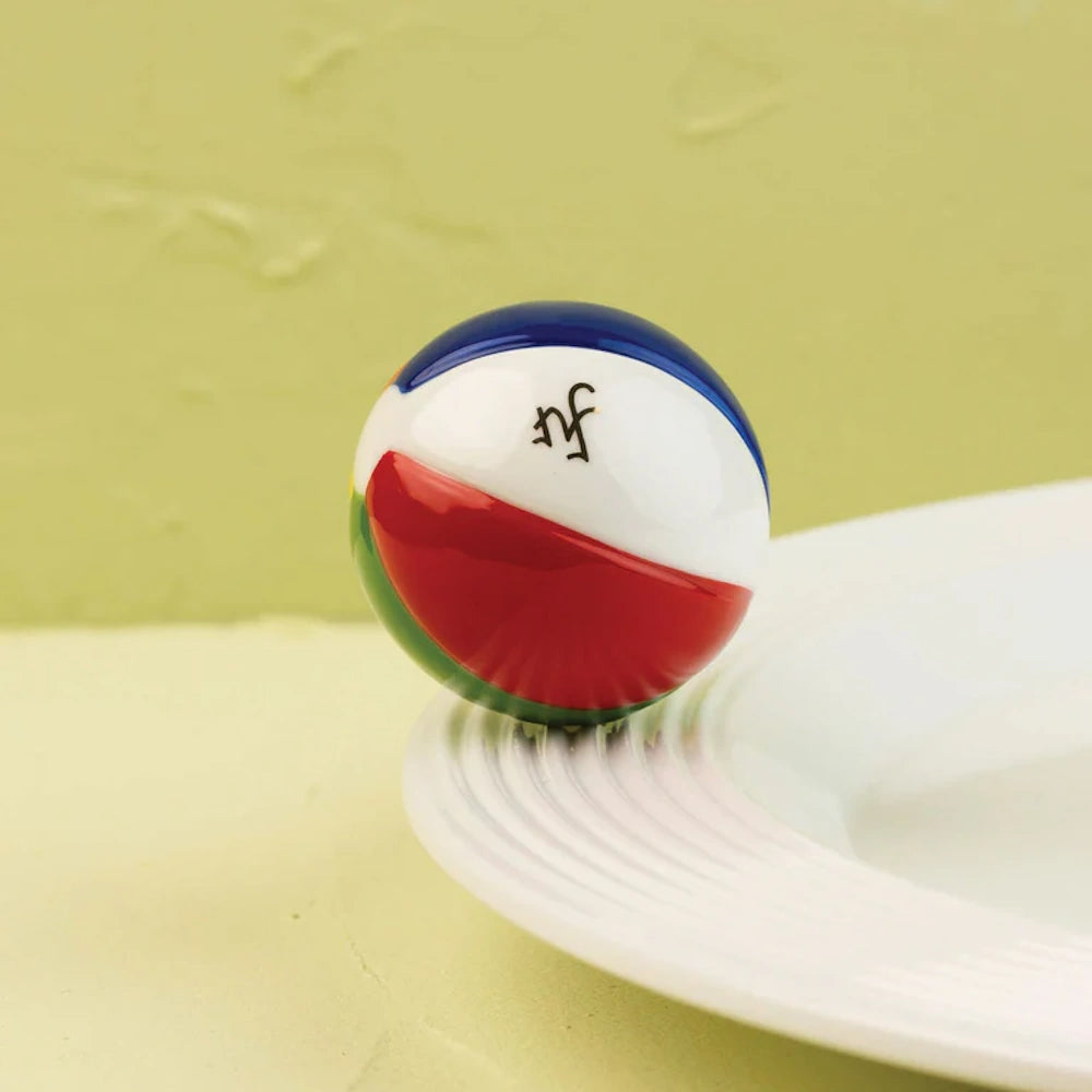 Glossy ceramic beach ball ornament with red, blue, green, and white panels resting on a white platter.