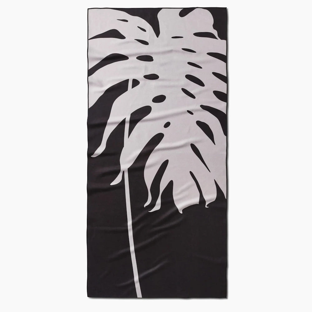 Black and white beach towel featuring a large graphic print of a monstera leaf.