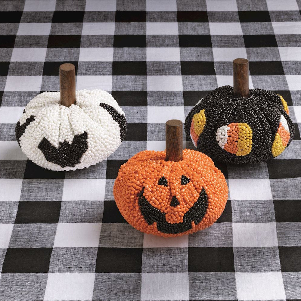 Three beaded decorative pumpkins on a black and white checkered tablecloth.