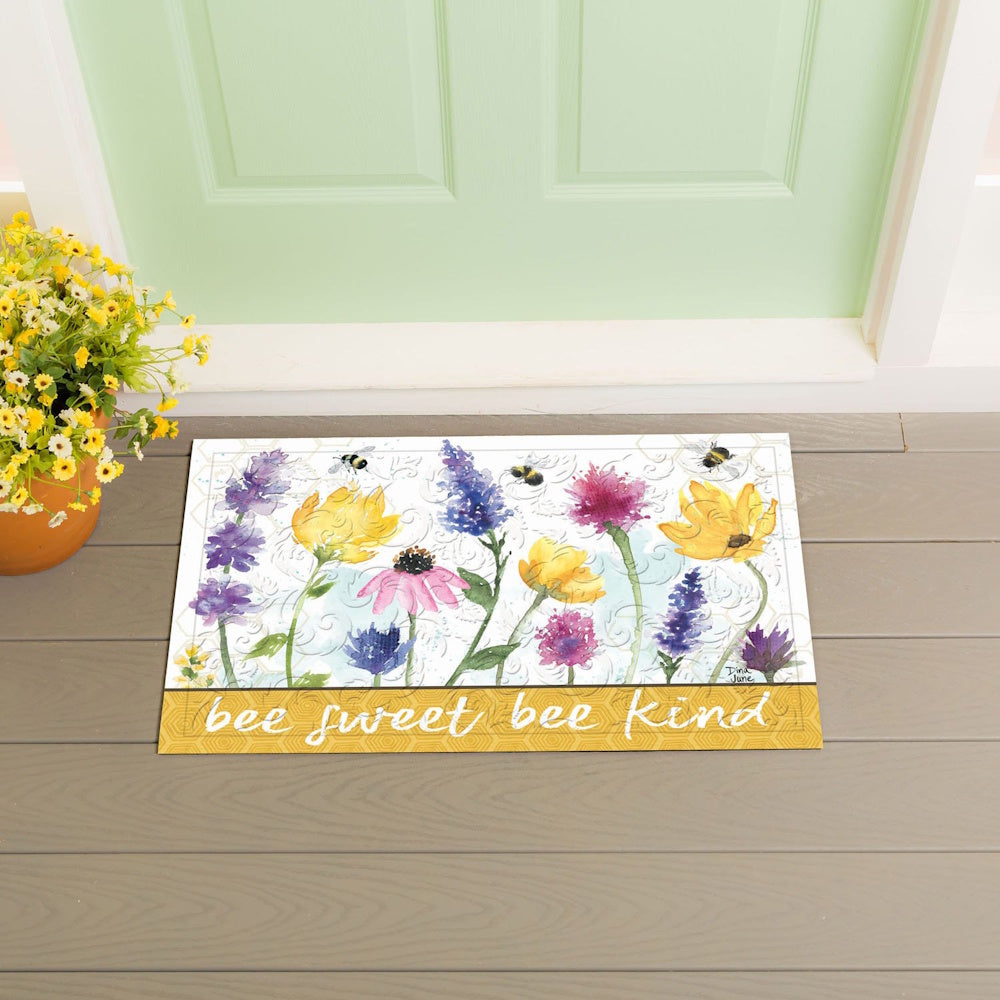 A floral doormat reading "bee sweet bee kind" sits on a porch in front of a light green door.