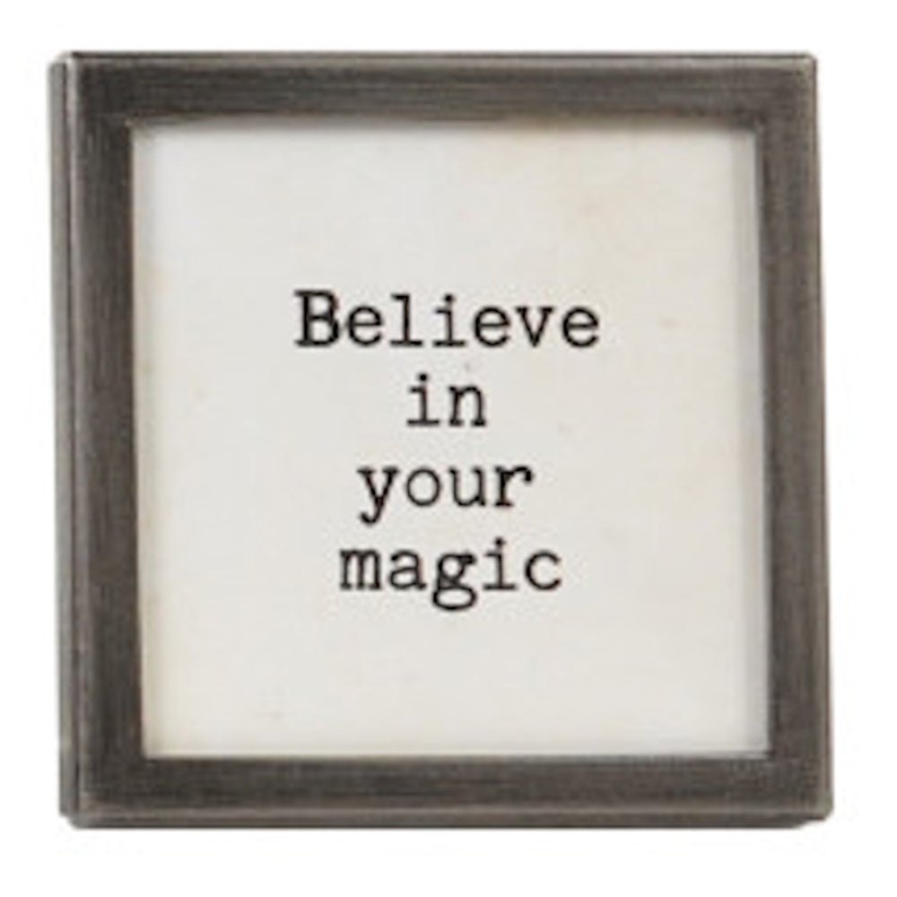 A square silver-framed sign with the text "Believe in your magic" in black typewriter font.