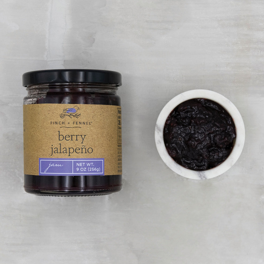 A jar of Finch + Fennel berry jalapeño jam next to a small marble bowl filled with dark jam.