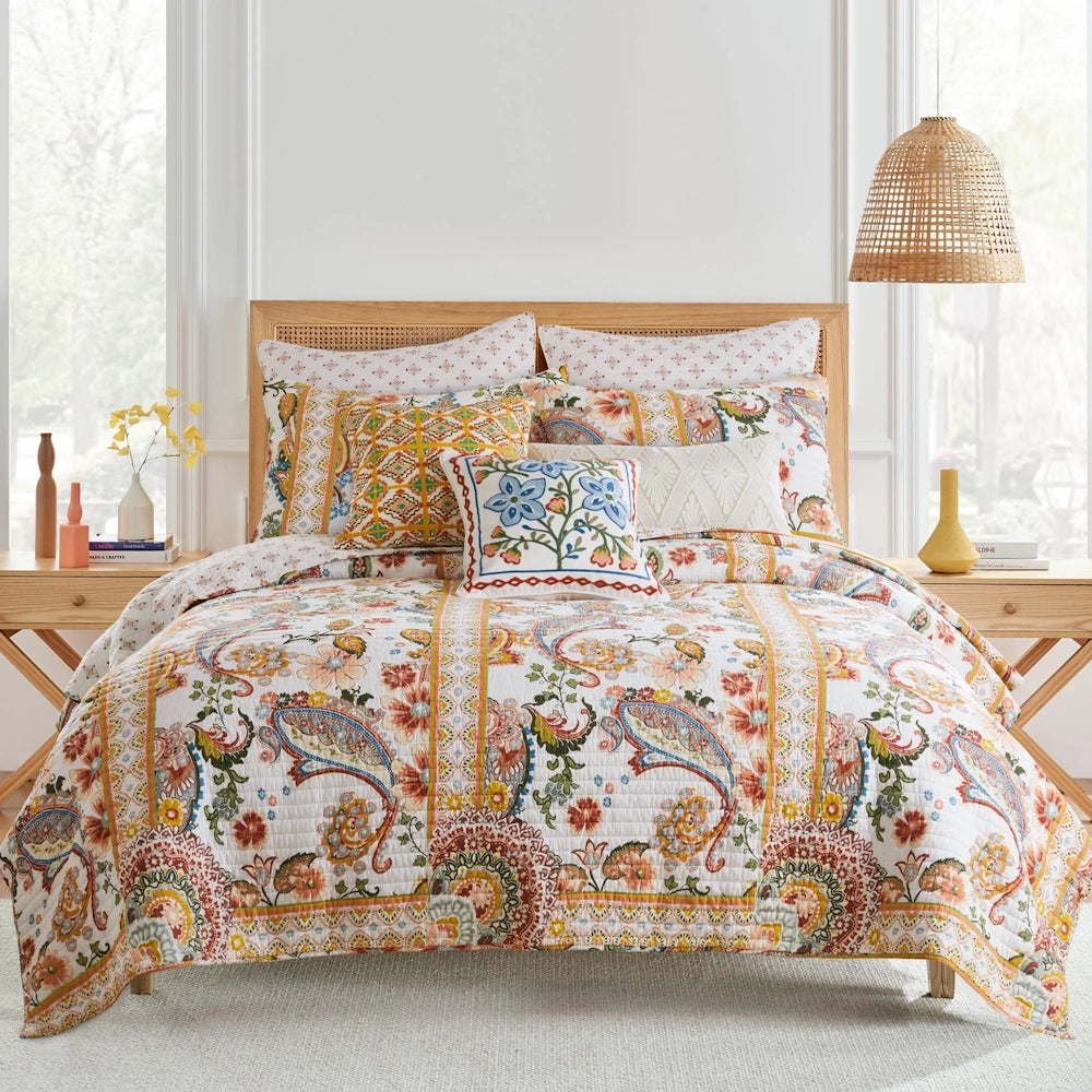 Bed styled with a colorful paisley quilt set, accent pillows, and wooden nightstands in a bright room.
