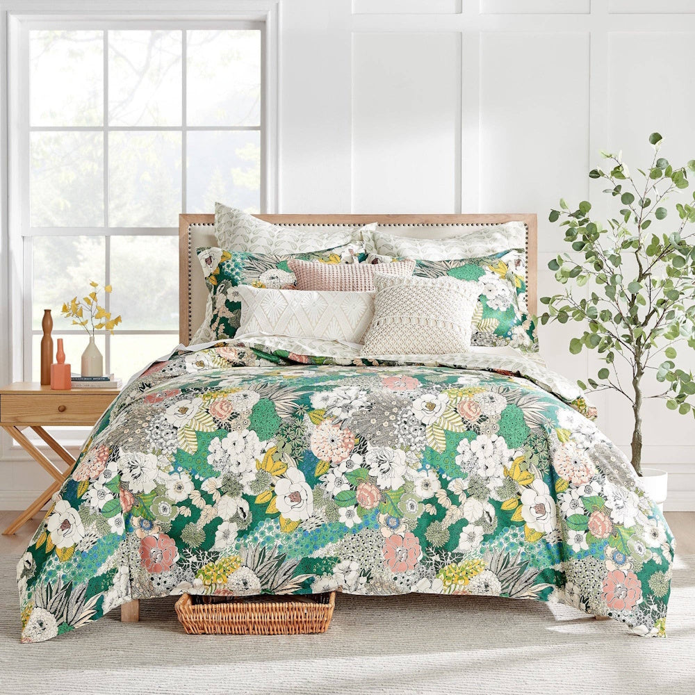 Bed set with a vibrant green, white, and pink floral comforter, matching shams, and decorative throw pillows.