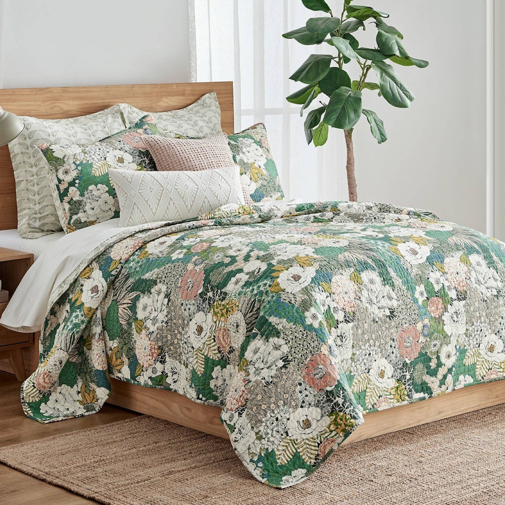 Bettina floral quilt set with green and pink botanical patterns on a wooden bed frame in a bright, modern room.